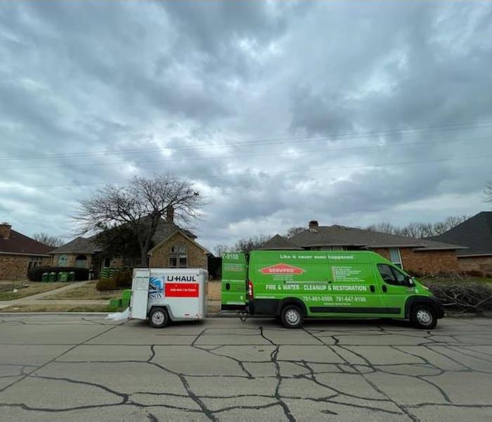 SERVPRO green van with UHAUL trailer parked in front of brick home